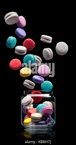 delicious French dessert macarons flying out from the glass jar on a black background Stock Photo
