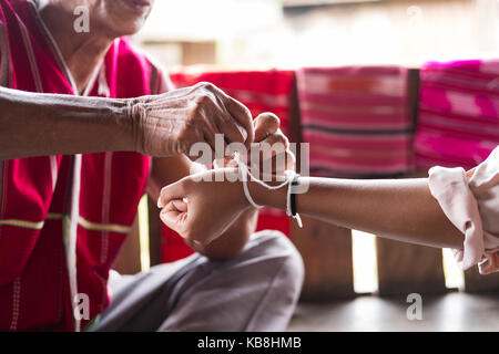 Chiang Mai, Thailand - September 14, 2017: Unidentified elder man from Karen ethnic hill tribe minority tie guest's wrist for blessing in tying ceremo Stock Photo