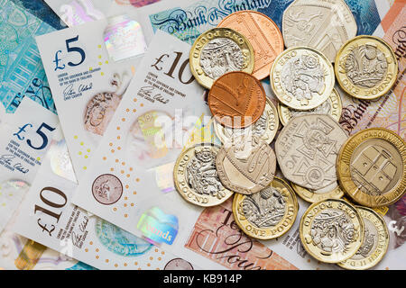 British UK money sterling £10 and £5 notes GBP and a pile of new issue pounds one pound coins cash. Saving money savings concept. England UK Britain Stock Photo