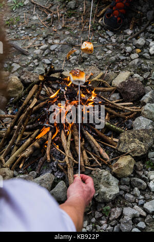Point-of-view shot of a woman toasting a marshmallow over an open campfire. UK Stock Photo
