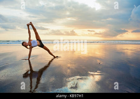 Sunset meditation. Young active woman stretching in yoga pose on sea beach  to keep fit and health. Healthy lifestyle, flexibility training, sport  activity in sport camp on summer family holiday. Stock Photo