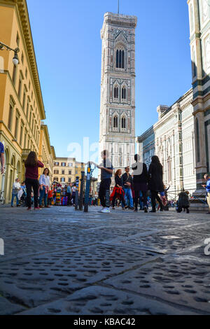 Tourists shop for gifts and take photographs at Piazza del Duomo with Giotto's Campanile in the background Stock Photo