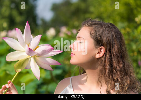 Portrait closeup of young woman face looking at bright white and pink lotus flower with yellow seedpod inside in garden, park Stock Photo