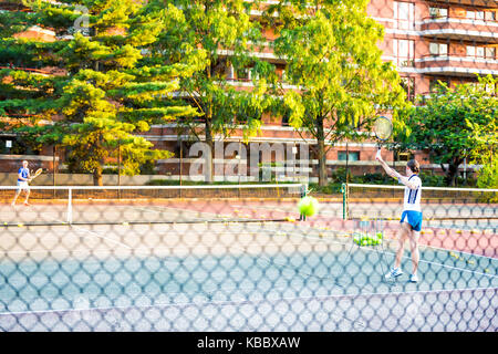 Washington DC, USA - August 4, 2017: Tennis players couple, man, woman playing, serving in Francis Stevens Playground park with ball in motion behind  Stock Photo