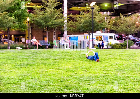 Washington DC, USA - August 4, 2017: People sitting on benches in green downtown Georgetown waterfront park neighborhood with young man lying on grass Stock Photo