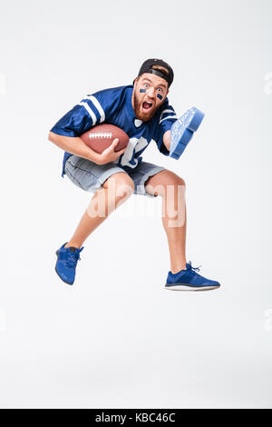 Image of screaming man fan in blue t-shirt jumping isolated over white background. Looking camera holding rugby ball. Stock Photo