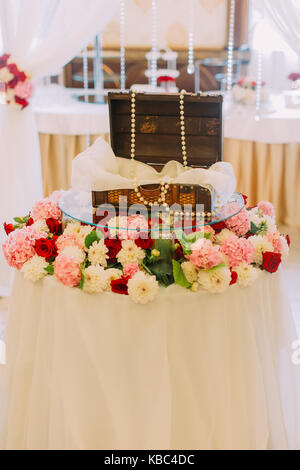 Wedding wooden box decorated with beads placed on the table covered with colourful flowers. Stock Photo