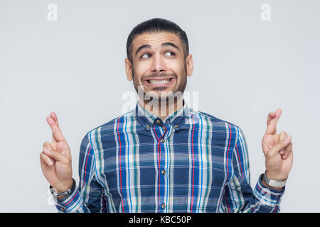 The very cunning businessman, crossing fingers for good luck, hoping wishes will come true, looking up slyly. Indoor, studio shot Stock Photo