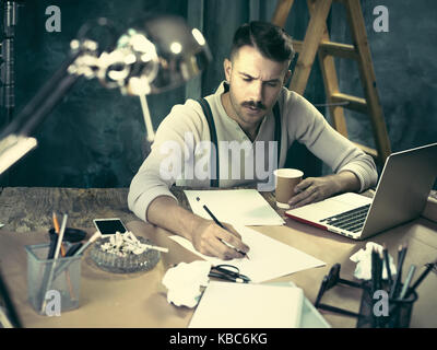 The handsome elegant man sitting at home table, working and using laptop while smoking cigarettes Stock Photo