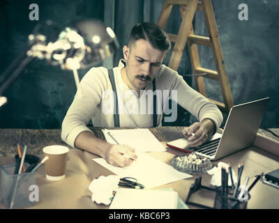 The handsome elegant man sitting at home table, working and using laptop while smoking cigarettes Stock Photo