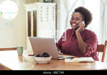 Smiling African woman talking on her cellphone and working online Stock Photo