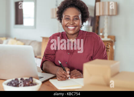 Smiling African woman writing in a notebook and working online Stock Photo