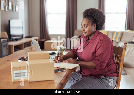 Young African woman working online and writing in a notebook  Stock Photo