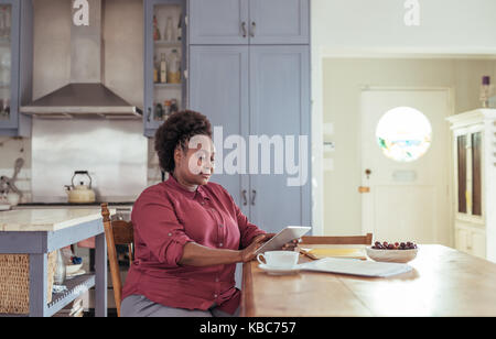 Focused African woman working on a tablet in her kitchen Stock Photo