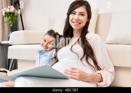 Girl and pregnant mother reading book Stock Photo
