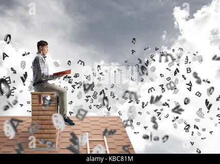 Man on brick roof reading book and symbols flying around Stock Photo