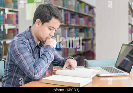 young student reading  book at library. Young asian man sitting at table with notebook computer in university library. knowledge, education and concep Stock Photo