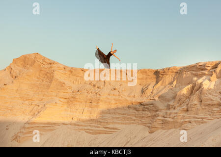 Woman dances high on a sand dune against the sky. Stock Photo