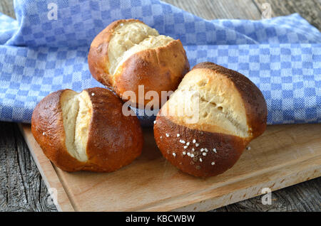 Three lye rolls on an old wooden table with a cutting board and a tea towel Stock Photo