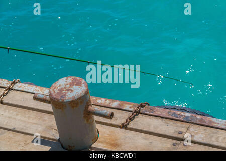 Old, rusty bollard with metal chain on pier with water. Stock Photo