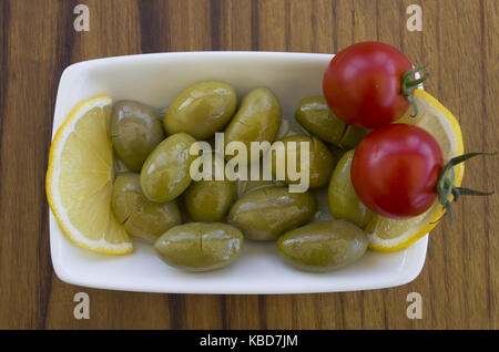 Green olive plate; on a wooden table with lemon slices and cherry tomatoes Stock Photo