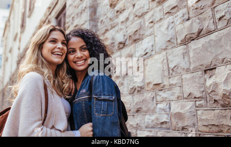 Young women standing together beside a stone wall. Two smiling women posing for a photograph outdoors. Stock Photo