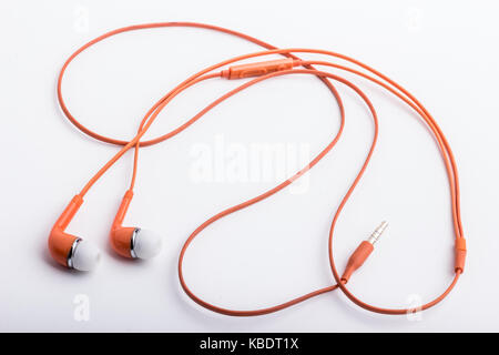 An orange used, stereo hands free set, lying on a white surface. Stock Photo