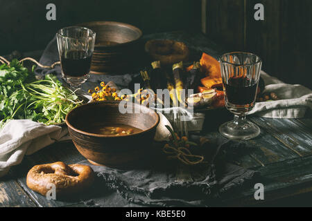 Fall holiday table decoration setting with bowls of hot carrot potato soup, baking pumpkin, carrot, garlic, fresh coriander, pretzels bread, red wine, Stock Photo