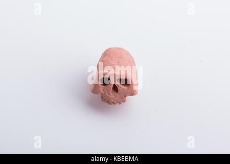 A part of an ugly skull made from orange clay, with it's jaw missing, on a white surface. Stock Photo