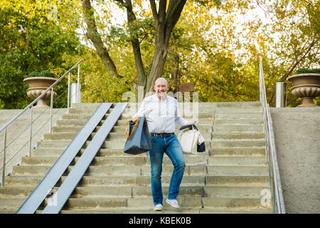 bald man with smiling happy face descending the stairs and holding shopping bag Stock Photo