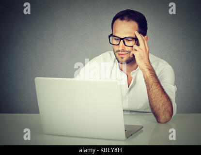 Closeup of a pensive businessman wearing glasses sitting at desk working on his laptop Stock Photo