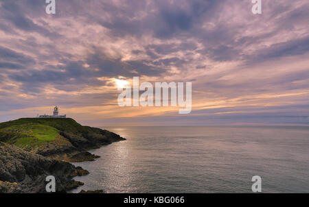 Spectacular evening sunset at Strumble Head, Pembrokeshire. Distant lighthouse on headland and dramatic clouds in sky. Stock Photo