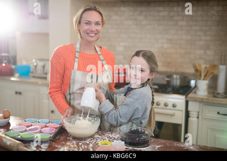 Portrait of smiling mother and daughter mixing eggs and wheat flour in a bowl Stock Photo