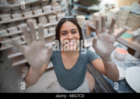 Portrait of female potter showing her hands with clay in pottery workshop Stock Photo