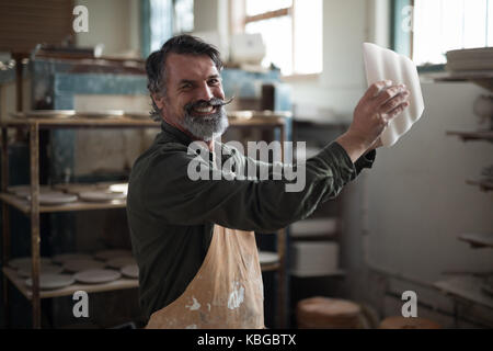 Portrait of male potter checking ceramic bowl in pottery workshop Stock Photo