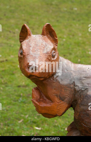Portrait, close-up shot of grumpy-looking squirrel wood carving, facing forward, standing on grass in a UK public park. Stock Photo