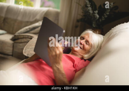 Senior woman using digital tablet on sofa in living room Stock Photo