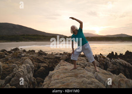 Senior woman doing exercise on seaside rocks during sunset Stock Photo