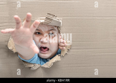 Zombie child boy screaming and reaching hand through hole on cardboard. Halloween day concept. Copy space. Stock Photo