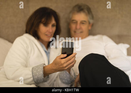 Senior couple smiling while using mobile phone in bedroom Stock Photo