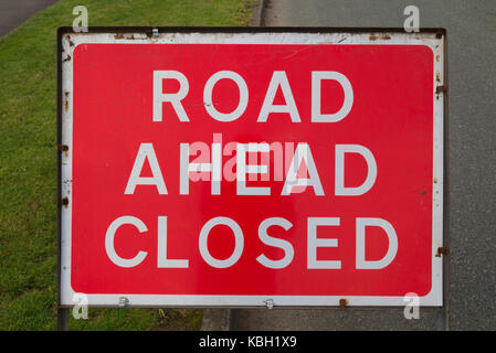 Large Road Ahead Closed sign. White on red background with grass and road behind Stock Photo