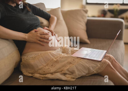 Mid-section of pregnant woman using laptop at home Stock Photo