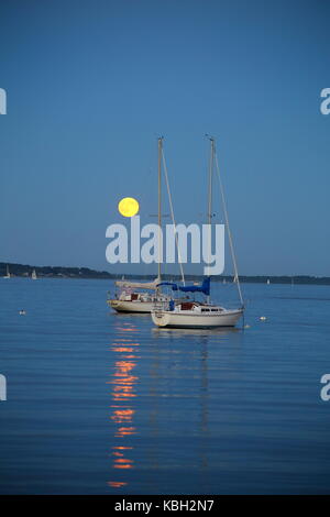 Full Harvest moon rising over Narragansett bay, in Rhode Island, Southern New England on a beautiful evening with sail boats in the water Stock Photo