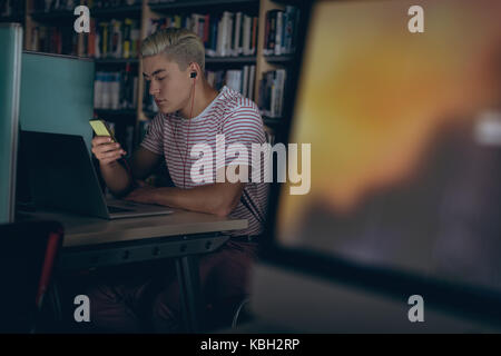 Man using listening music on headphones at desk in library Stock Photo