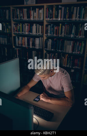 Man using desktop pc while listening music on headphones in library Stock Photo