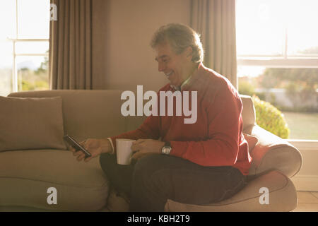 Senior man using phone on the couch in the morning light Stock Photo