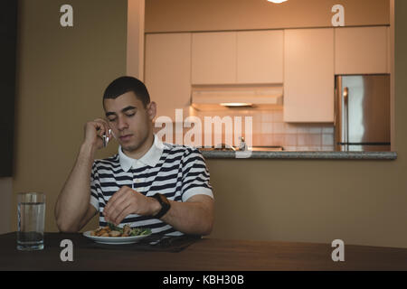 Man talking on mobile phone while having meal at home Stock Photo