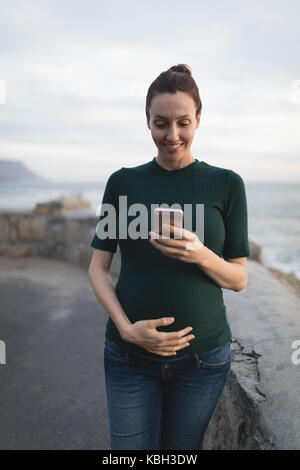 Happy pregnant woman using mobile phone outdoors Stock Photo