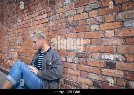 Man using mobile phone against brick wall Stock Photo