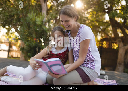 Smiling granddaughter and grandmother reading book in garden on a sunny day Stock Photo